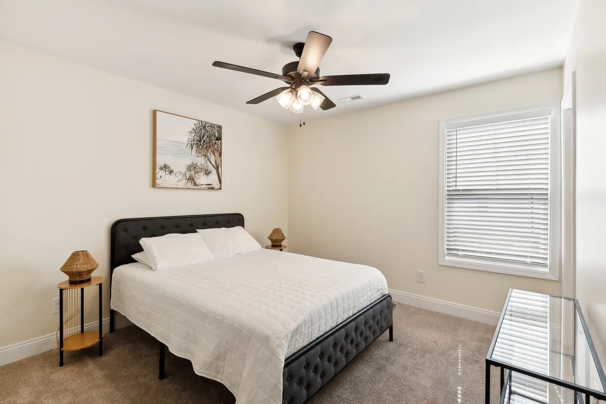 A tranquil bedroom scene featuring a neatly made bed with plush bedding, flanked by matching nightstands, stylish wall art, and a sunlit window. The overall design is modern with calming colors and a sense of comfort.