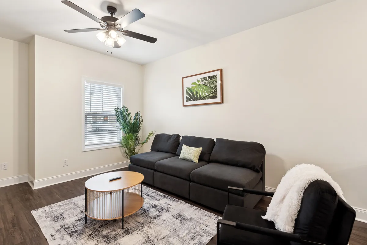 A cozy living room featuring a comfortable sofa, a coffee table, wall art, and a potted plant. The soft lighting and inviting arrangement create a welcoming atmosphere, ideal for unwinding or informal meetings.