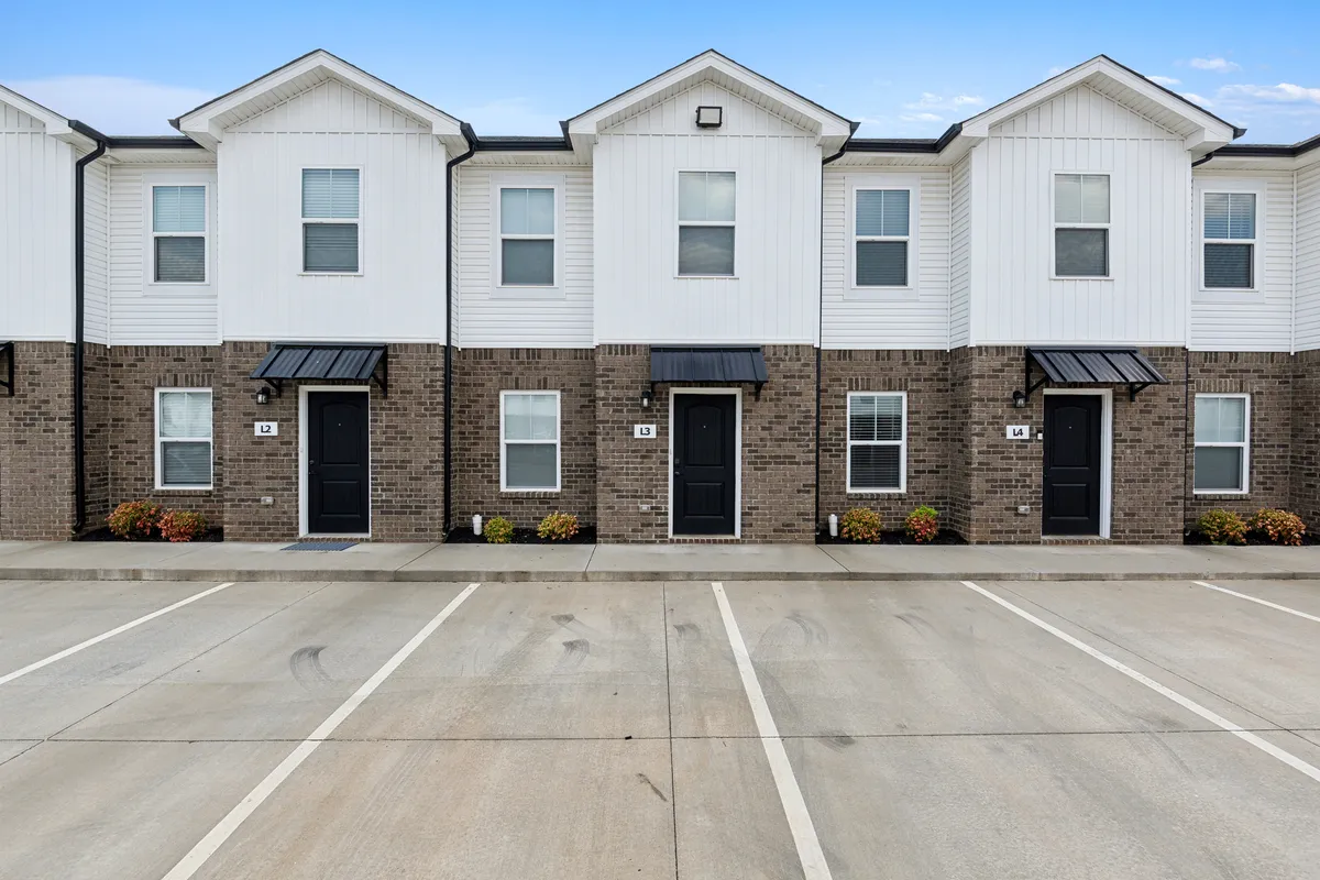 A welcoming exterior view of modern townhome architecture with a symmetrical layout and inviting front doors. The scene suggests a sense of community, outdoor leisure, and gatherings, with plenty of space in front for children to play or parties to be hosted. The environment is friendly and approachable, emphasizing the communal aspect of the living area.