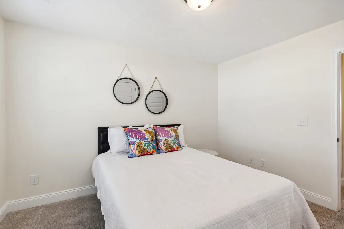 A tranquil bedroom scene with neatly made bed, decorative pillows, and mirrors, exuding an atmosphere of peace and rest. The arrangement suggests both comfort and style, ideal for restful nights or quiet reading sessions.