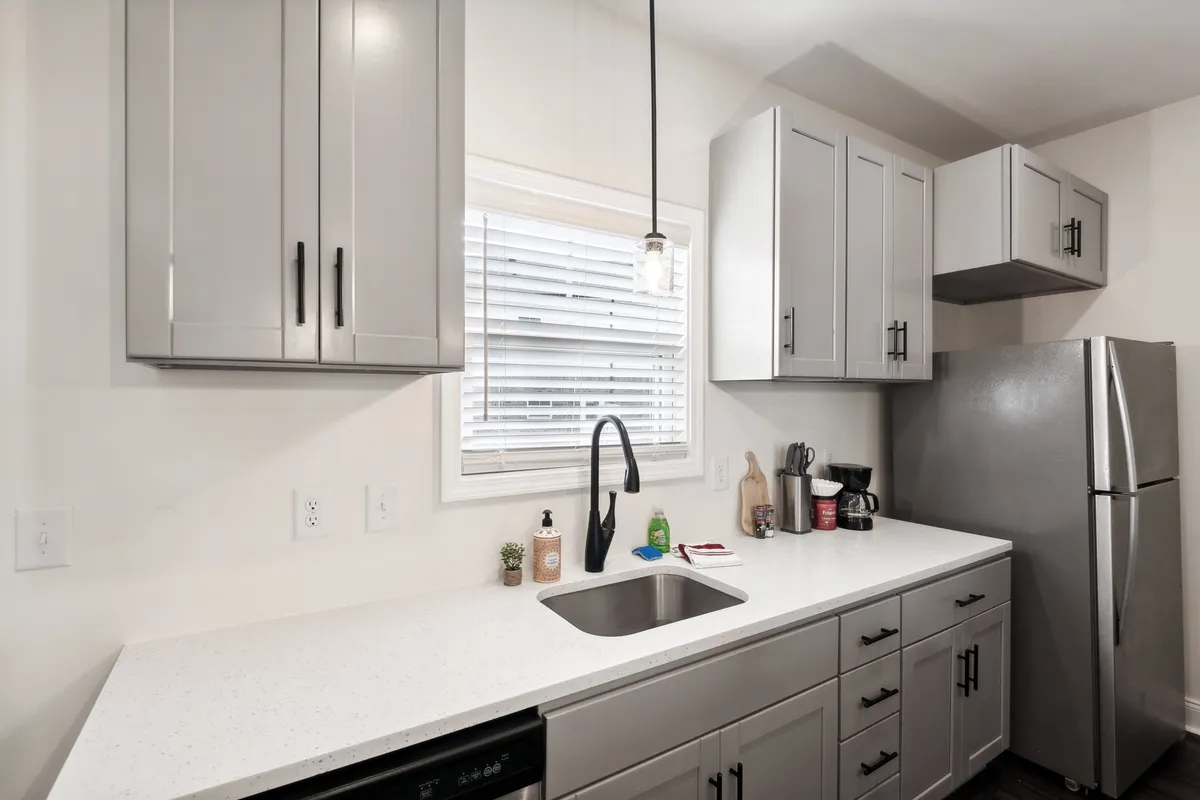 A bright, contemporary kitchen scene featuring a wide countertop, deep sink, stylish cabinets, and a stainless steel refrigerator. The clean lines and organized layout invite meal preparation and everyday gatherings.